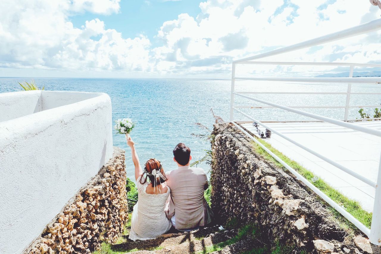 Rear view of bride and bridegroom sitting against sea