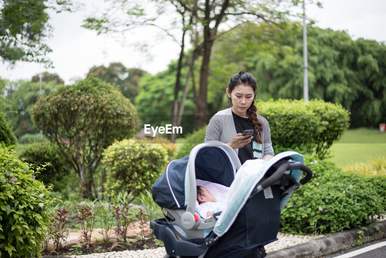 Woman using phone while standing by baby stroller at park