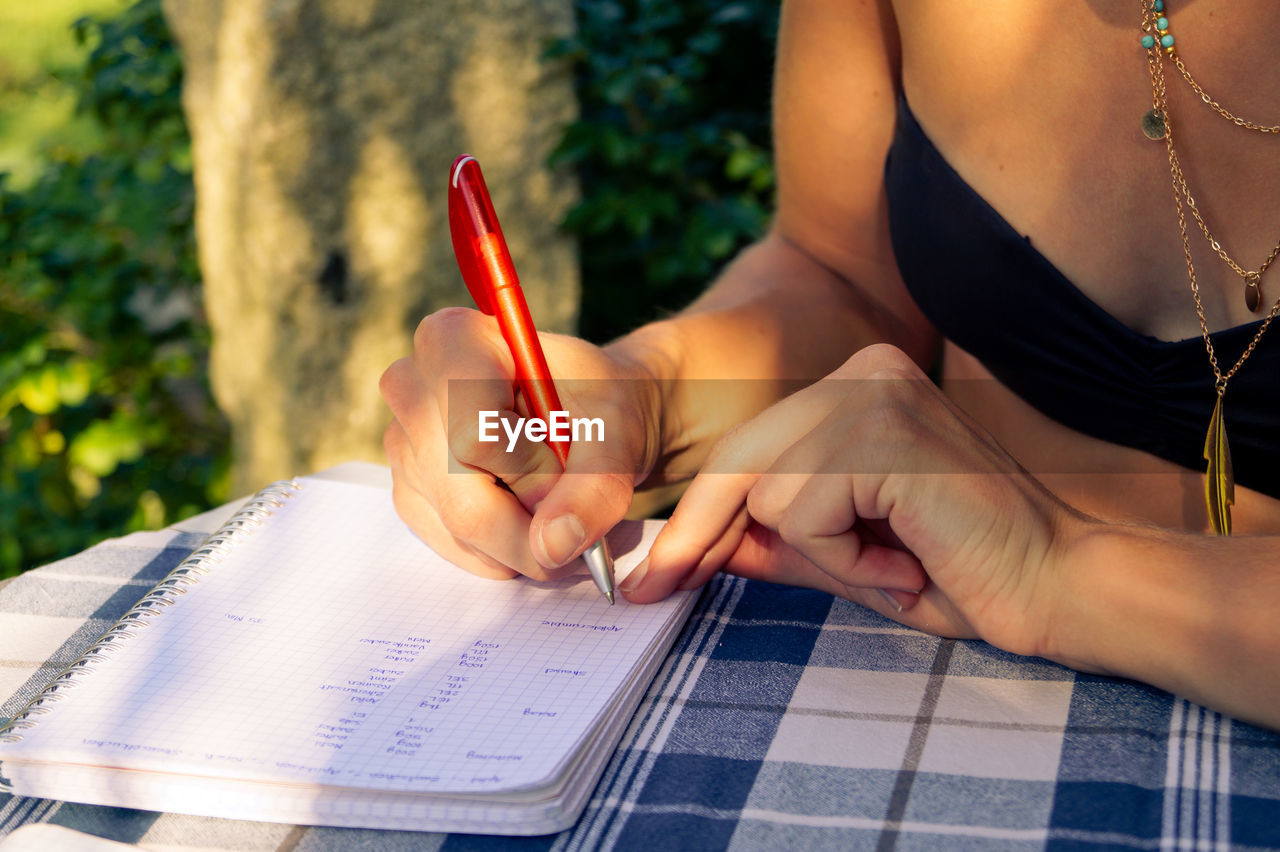 Midsection of woman writing on book at table