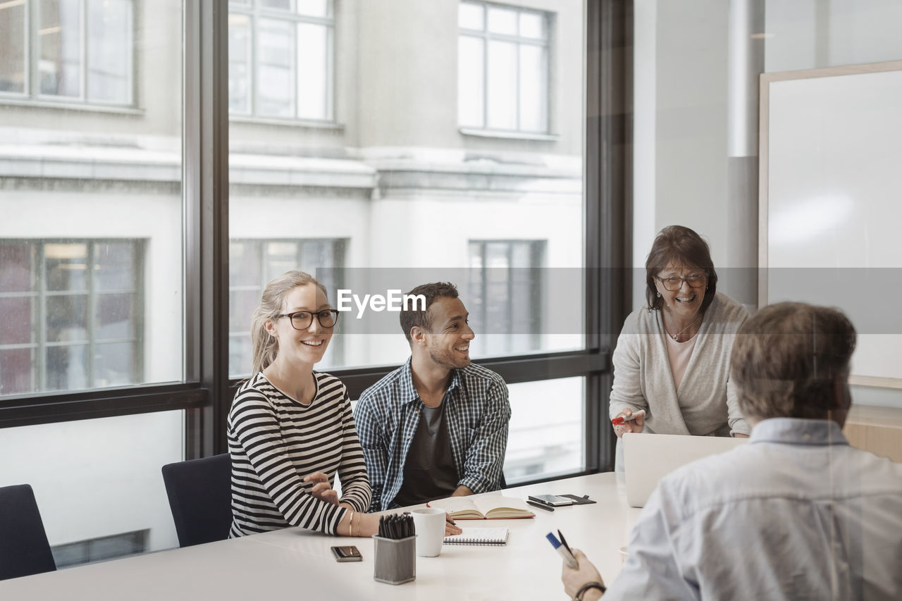 Happy businesswoman discussing with colleagues in board room