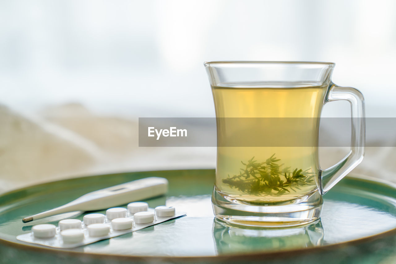 Glass transparent cup with herbal tea and grass leaves, thermometer, tablets. concept of health