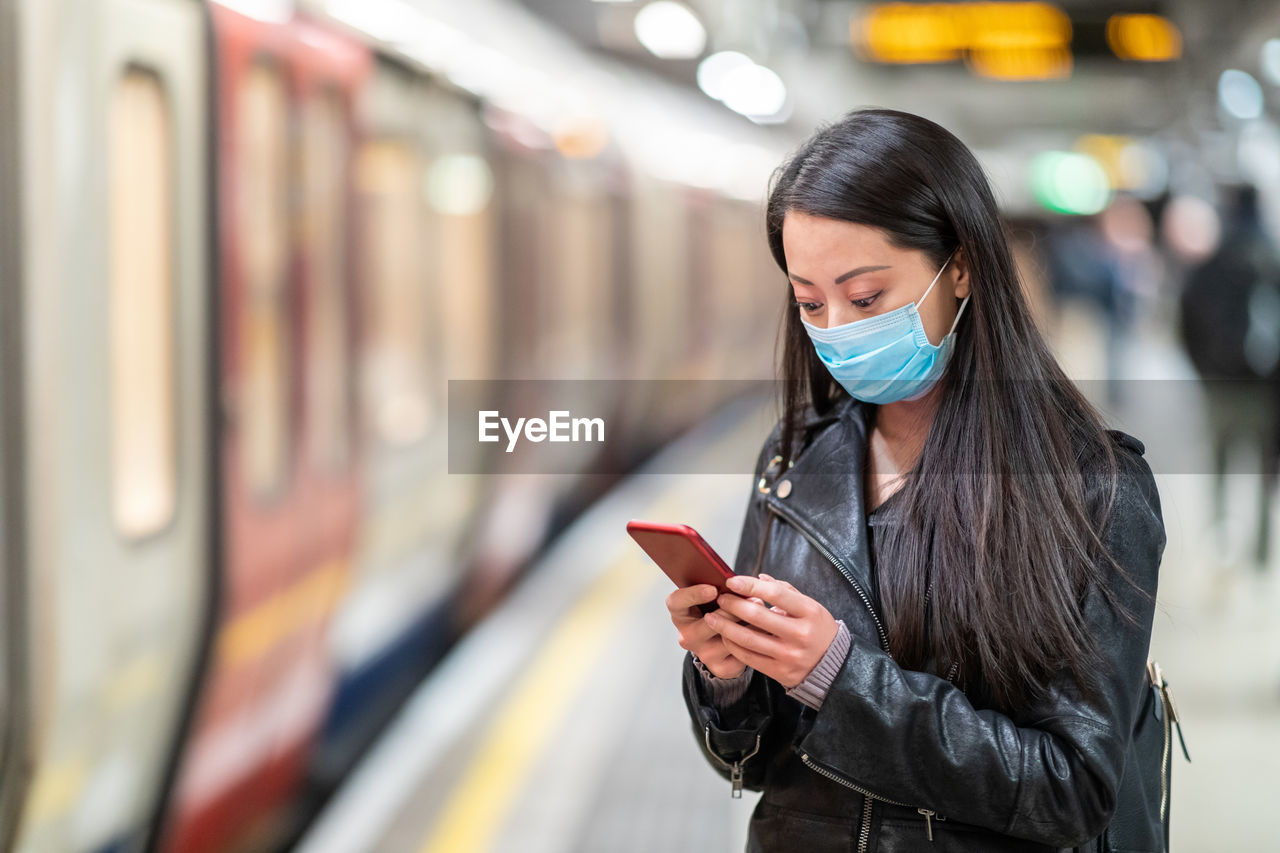 Woman wearing mask using smart phone on railroad station platform