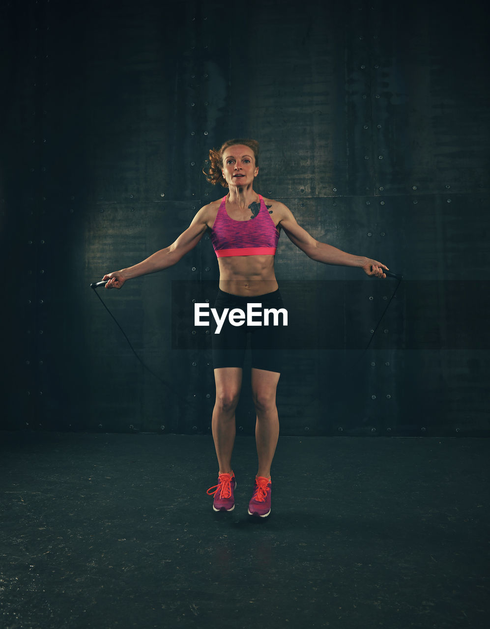 Full length portrait of woman exercising with jump rope at gym