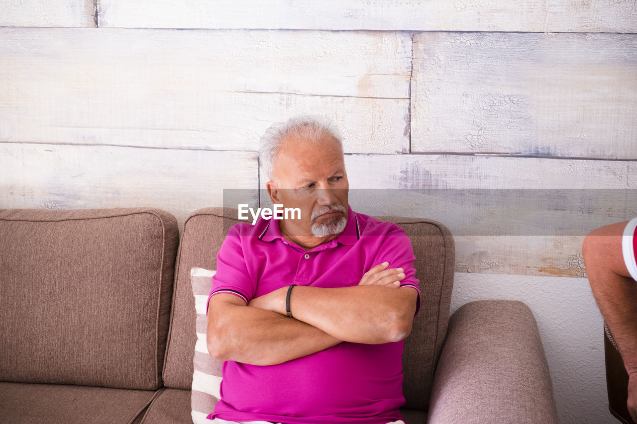 Senior man sitting on sofa against wall at home