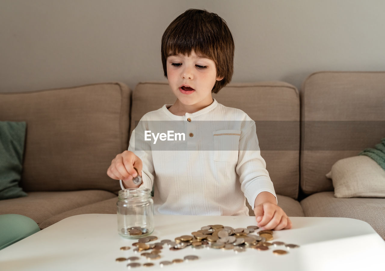 Little toddler boy counting money putting coins into glass jar. kid saving learn financial literacy