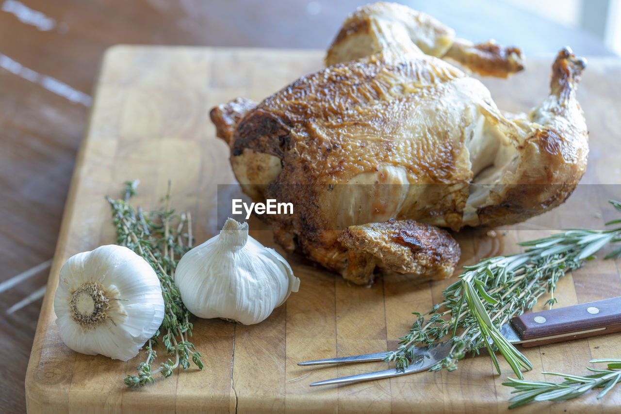 Rotisserie chicken served on a wood tray with garlic and rosemary.