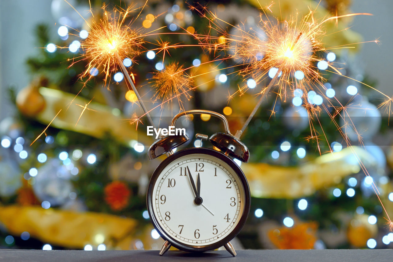 Close-up of alarm clock with sparklers against at night