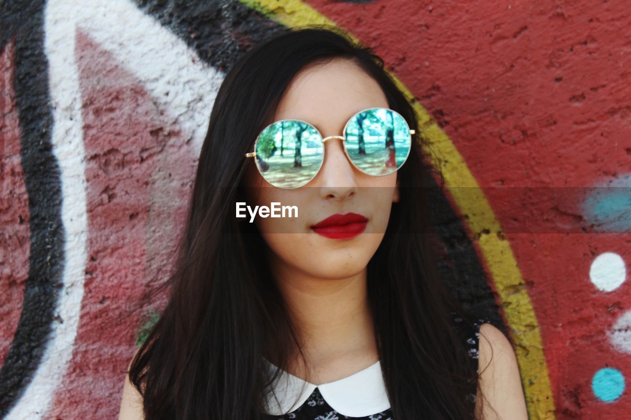 Young woman wearing sunglasses against wall