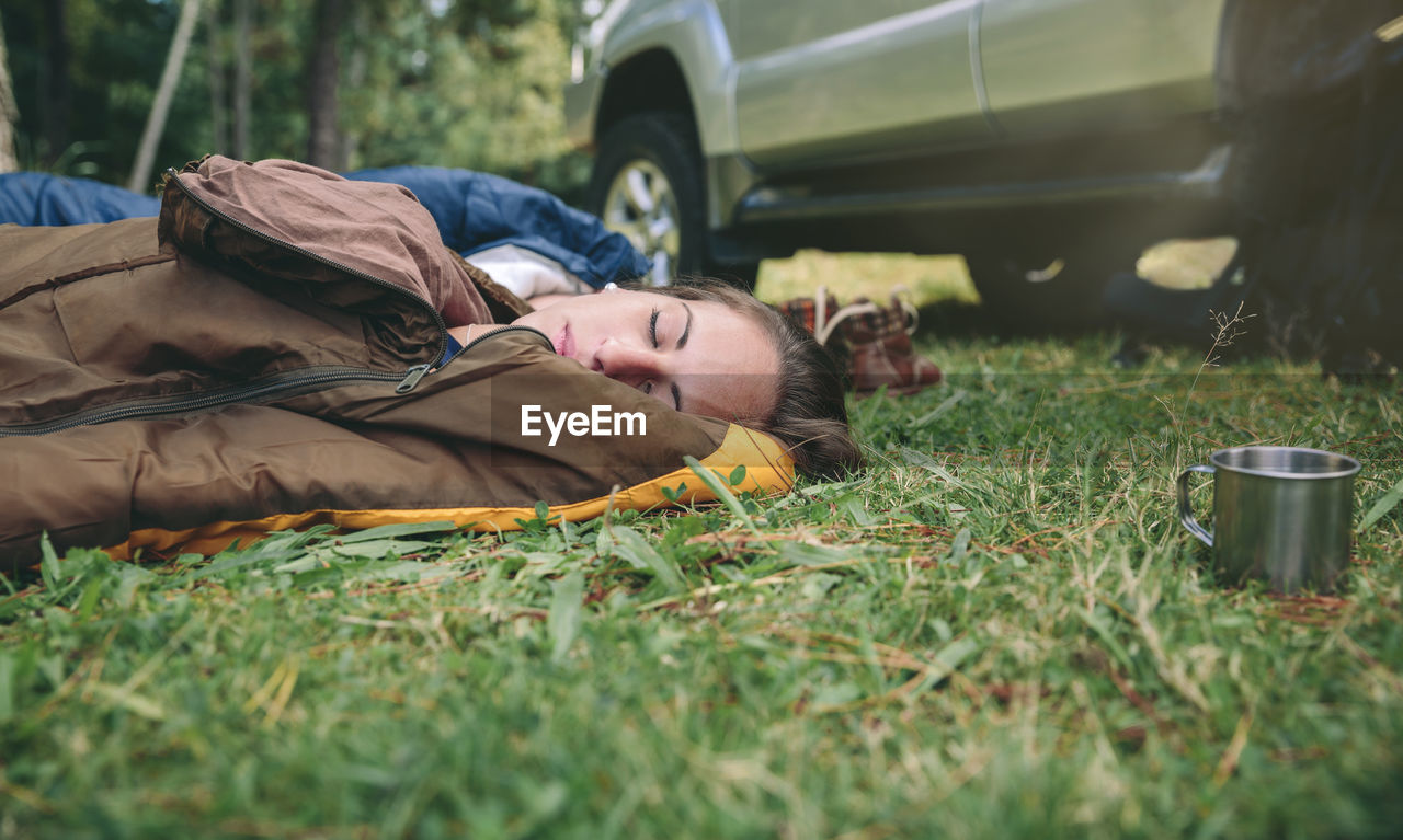 Woman napping in sleeping bags on grassy field