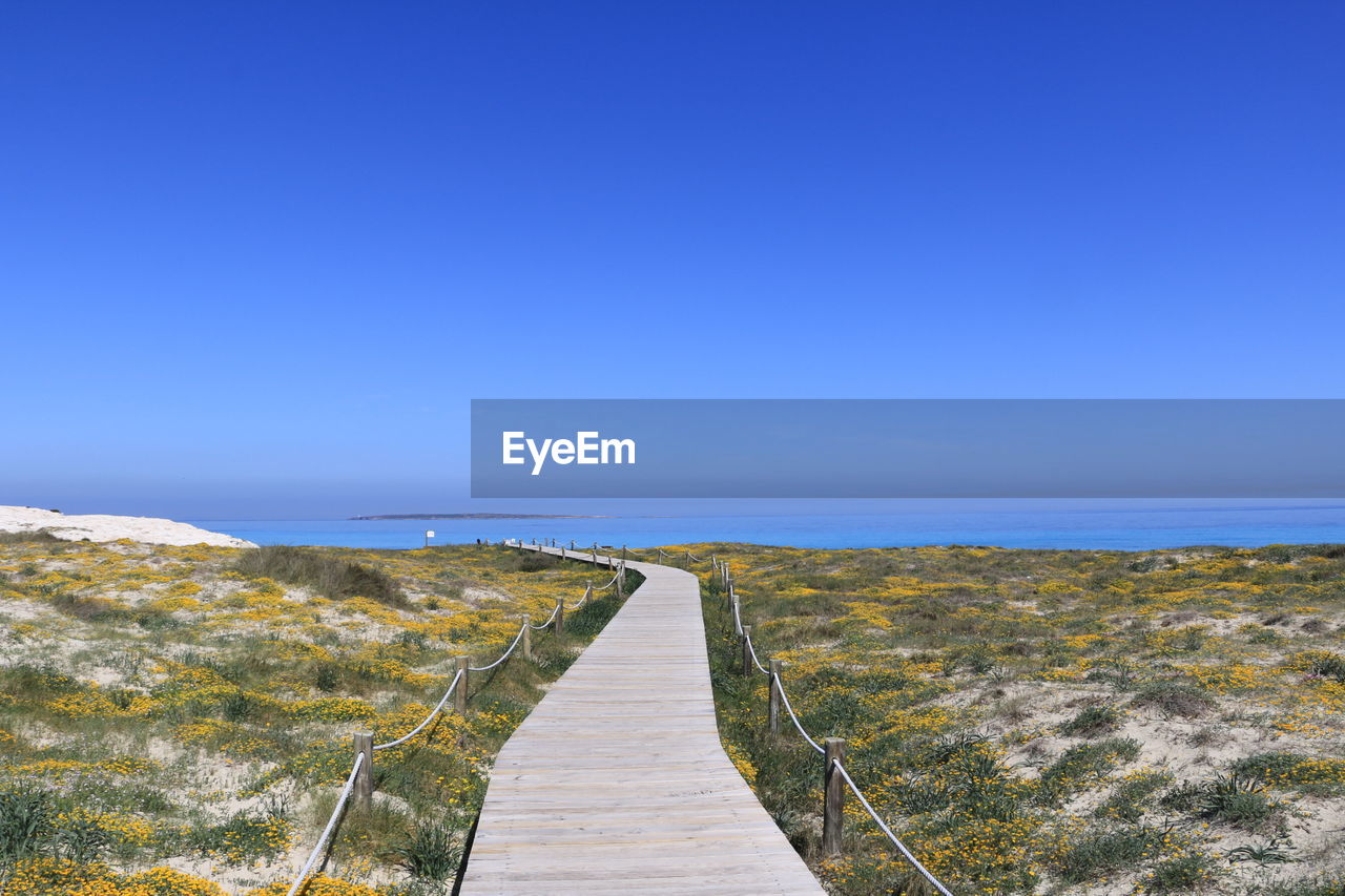 Walkway amidst sea against clear blue sky