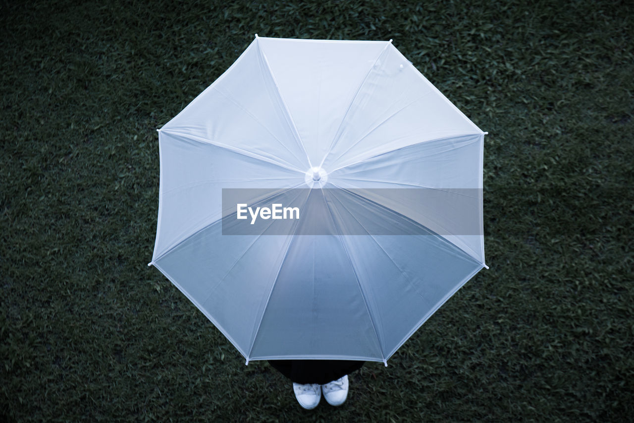 LOW SECTION OF PERSON STANDING ON FIELD BY UMBRELLA