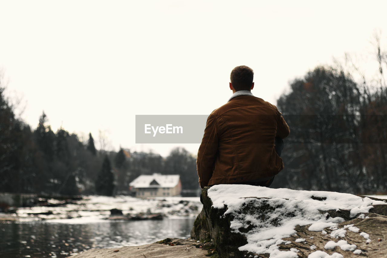 Rear view of man looking at lake against sky