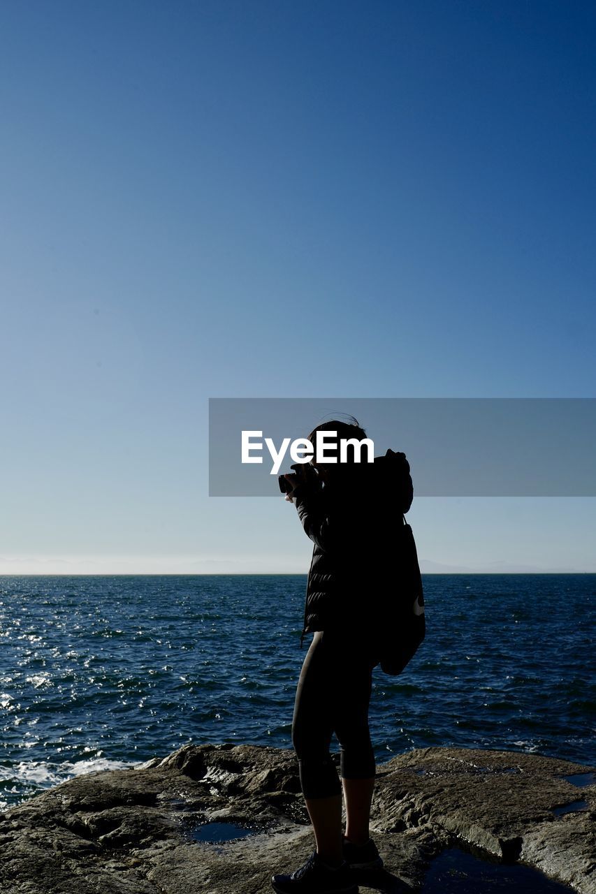 Rear view of woman standing at beach against clear blue sky