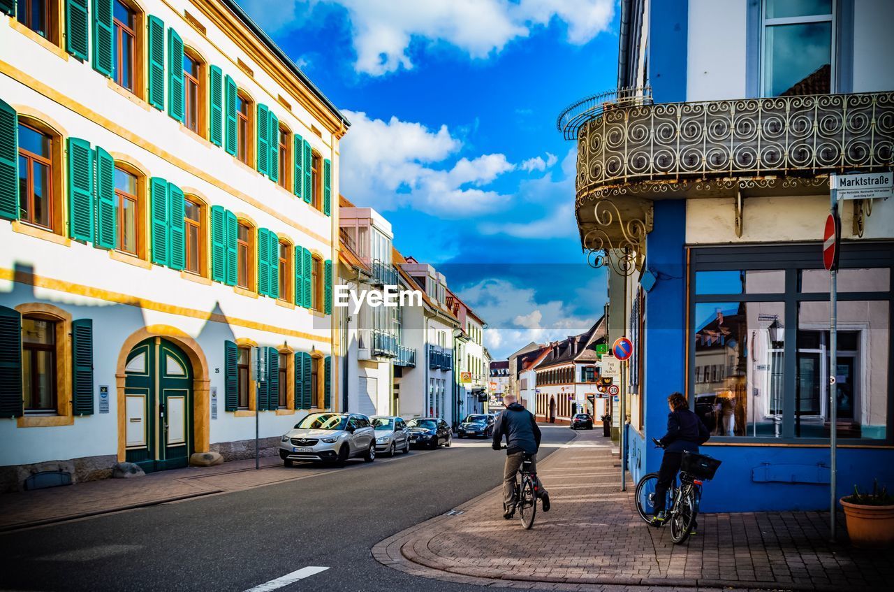 Man and woman with bicycles on footpath against buildings in city