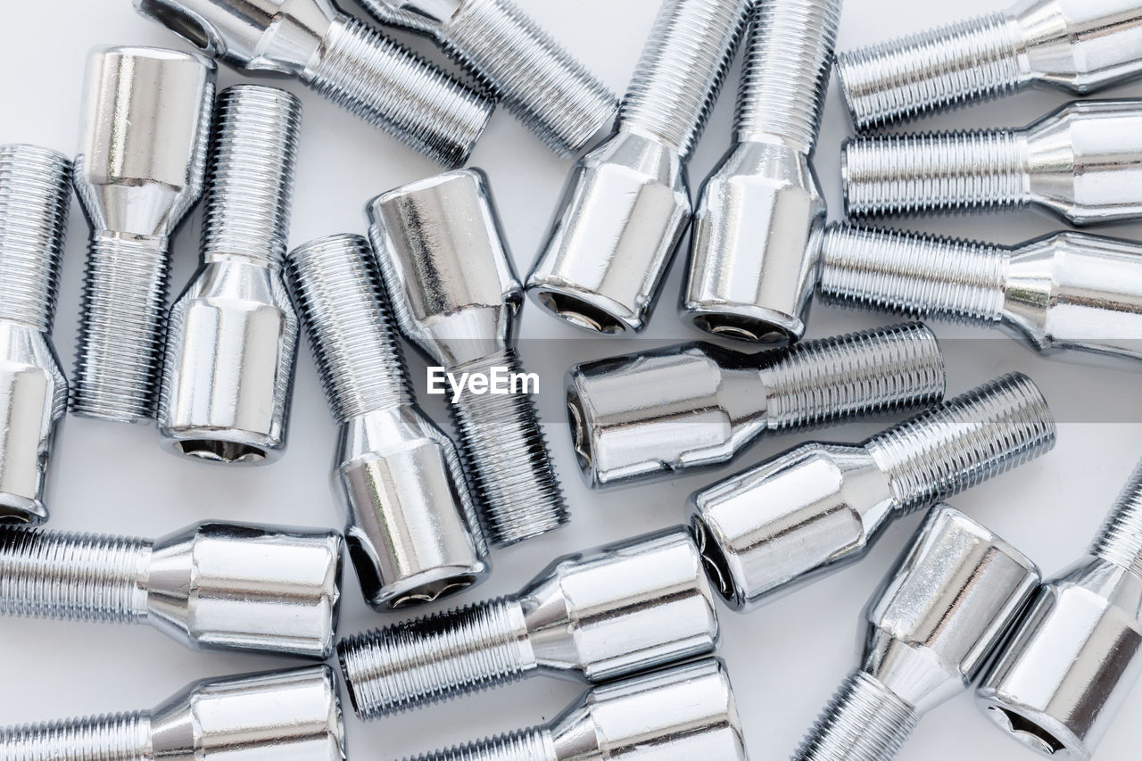 Shiny steel chrome coated wheel bolts on white background, full-frame closeup high angle view