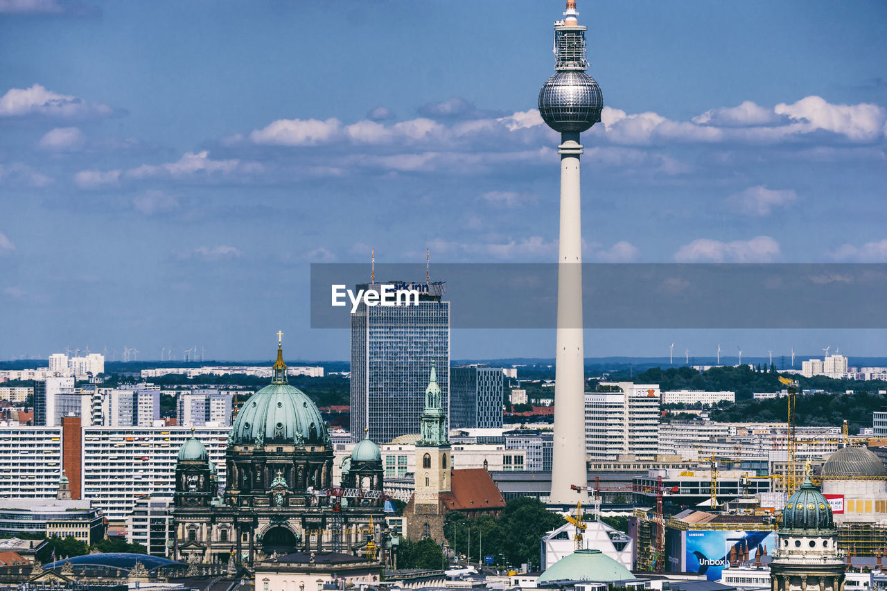 Aerial view of fernsehturm in city against sky during sunny day