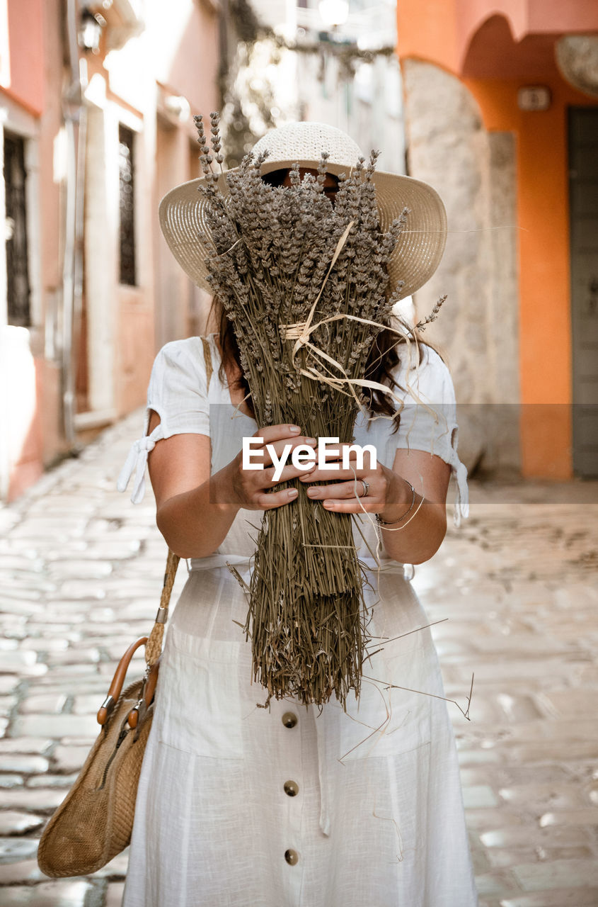 Front view of young woman holding dried lavender bundle in front of her face.