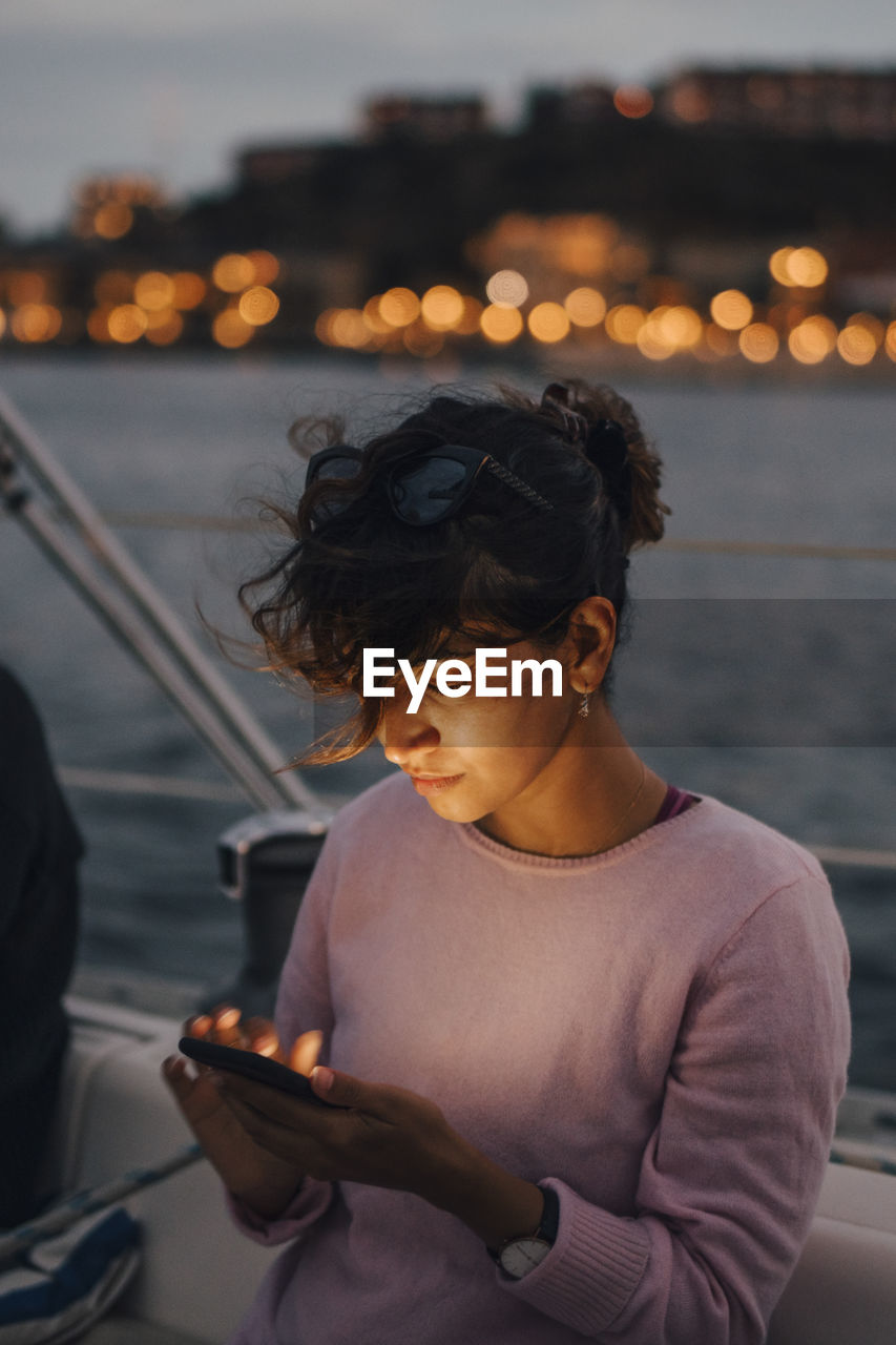 Mid adult woman using smart phone while sitting in boat during sunset