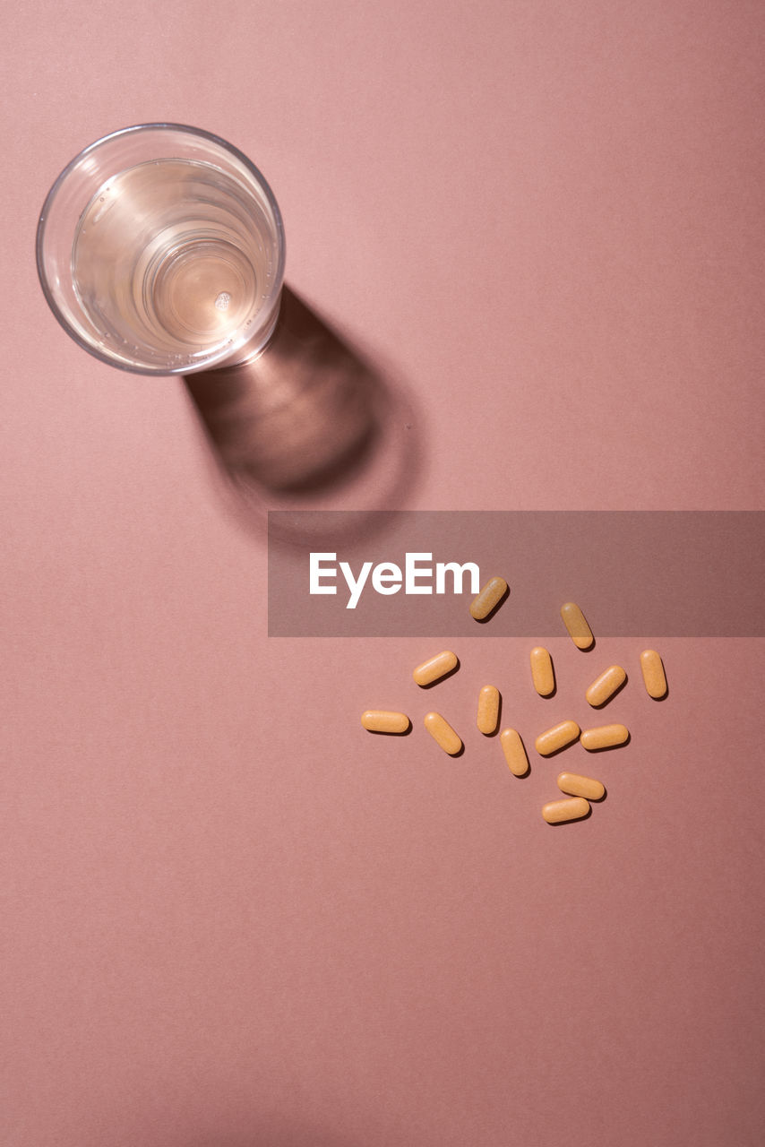Group of yellow pills and glass of water on a pink background, top view