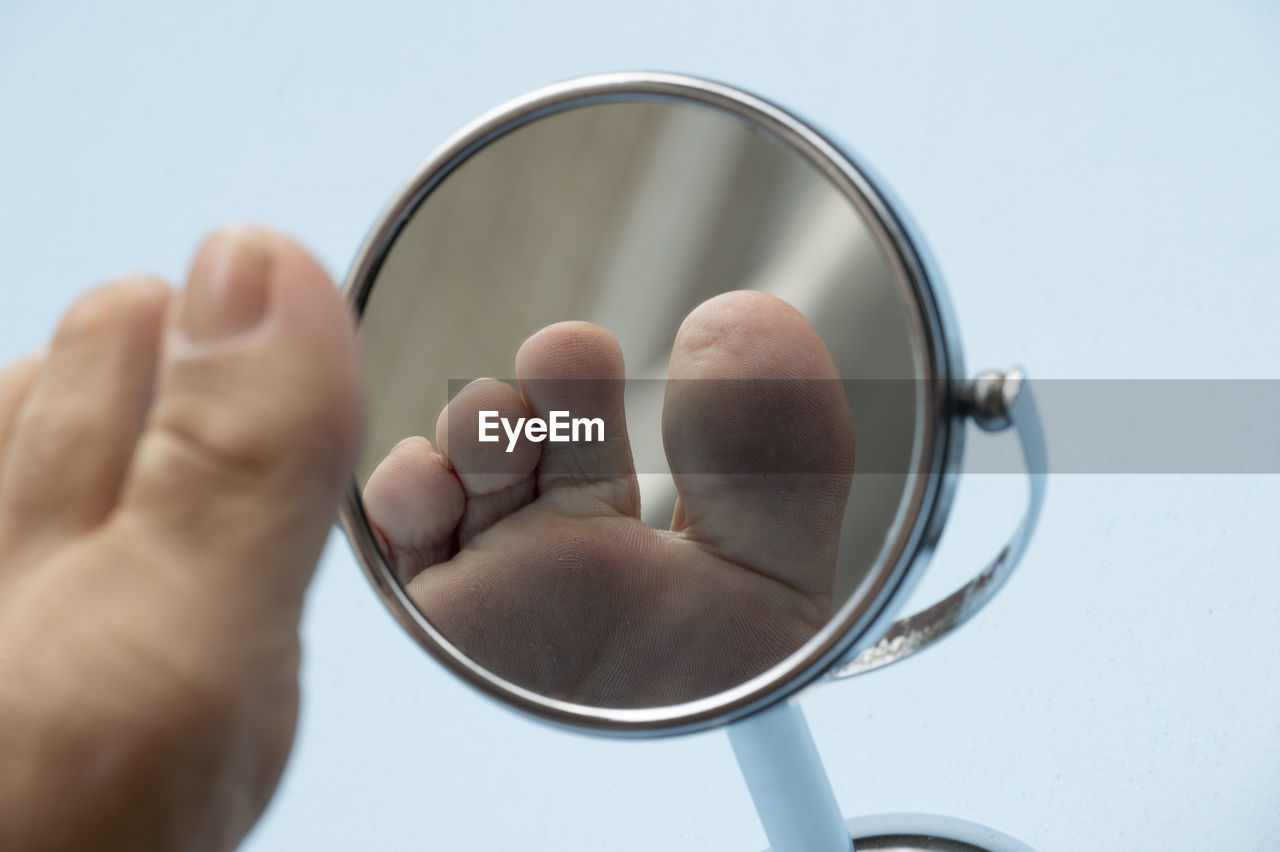 Low section of man by mirror against blue background