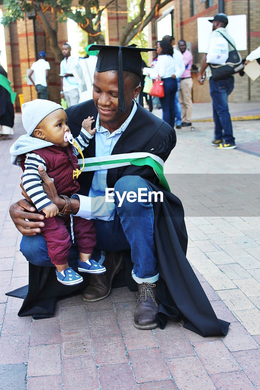 Father wearing graduation gown with toddler son at university