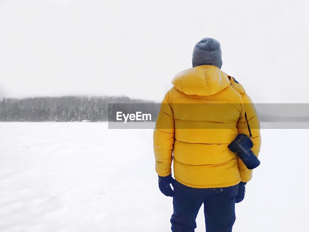 Rear view of man with digital camera standing on snowcapped field