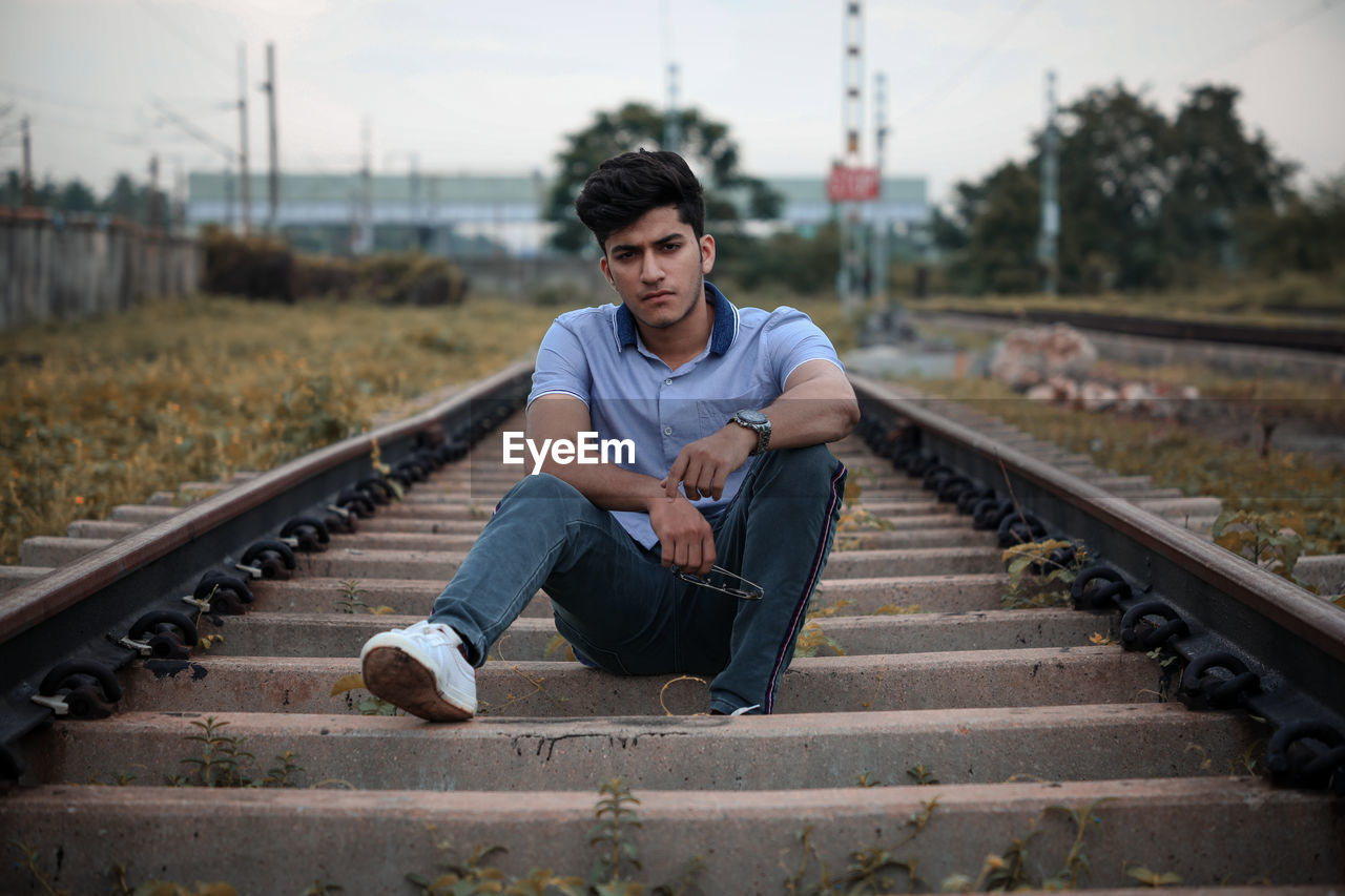 Portrait of young man sitting on railroad track