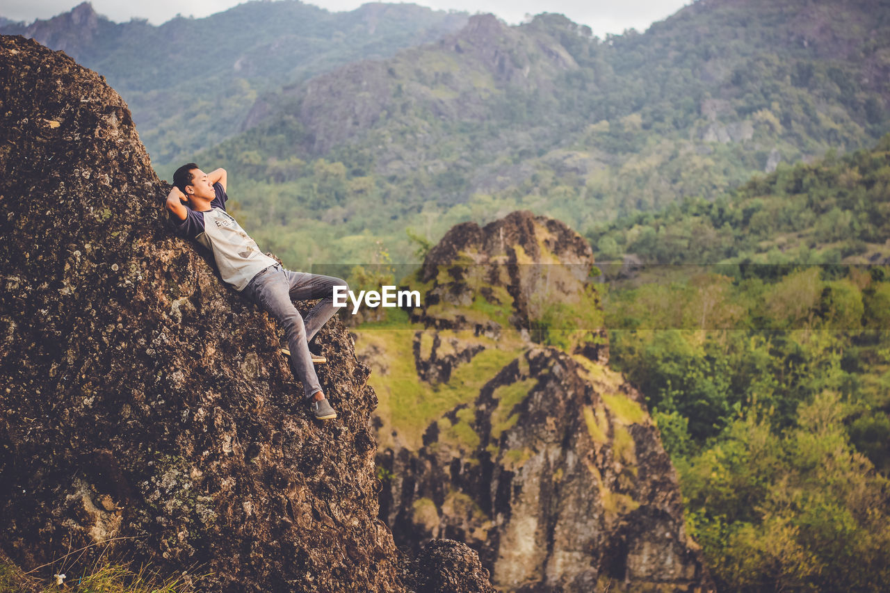 Side view of young man lying on rock formation