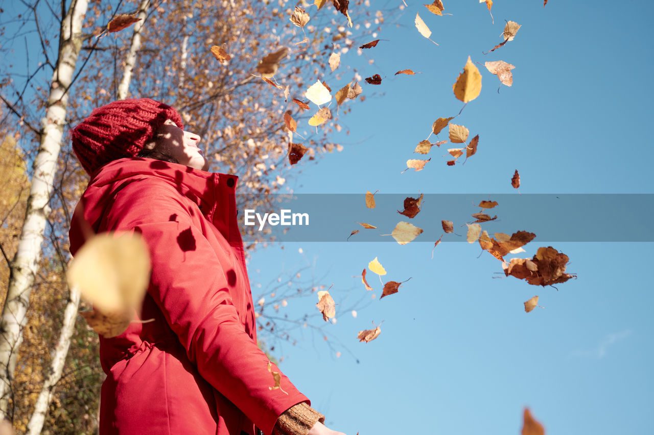 A woman in a red jacket throws yellow leaves. autumn landscape. slow motion video.