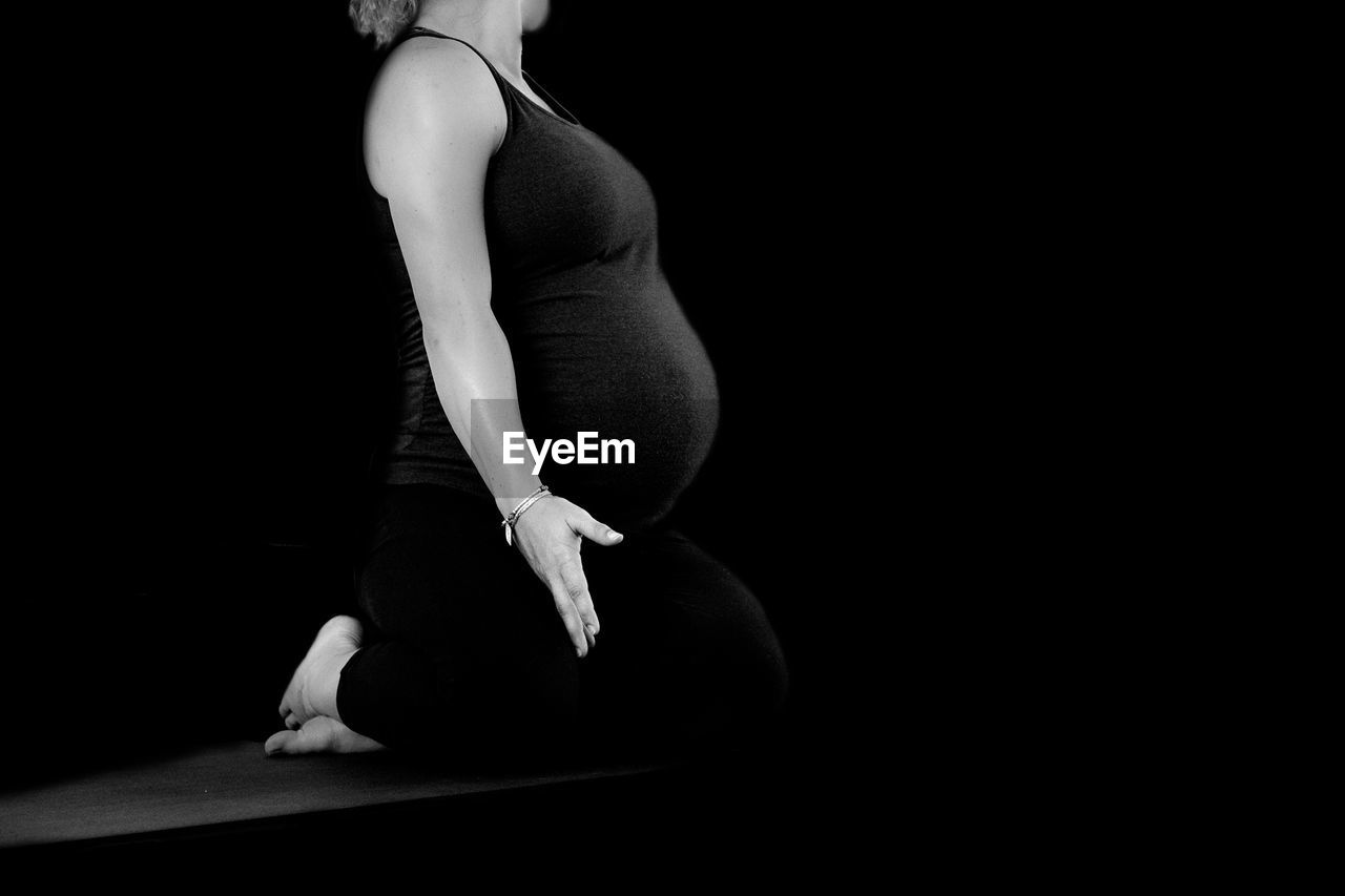 MIDSECTION OF WOMAN TOUCHING BLACK BACKGROUND