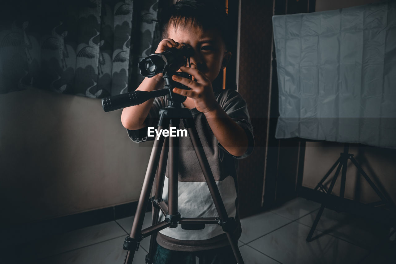 Boy using binoculars while standing on floor at home