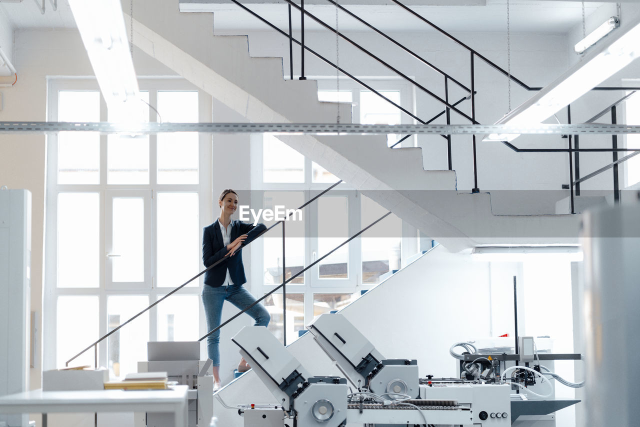 Female business professional leaning on railing in workshop