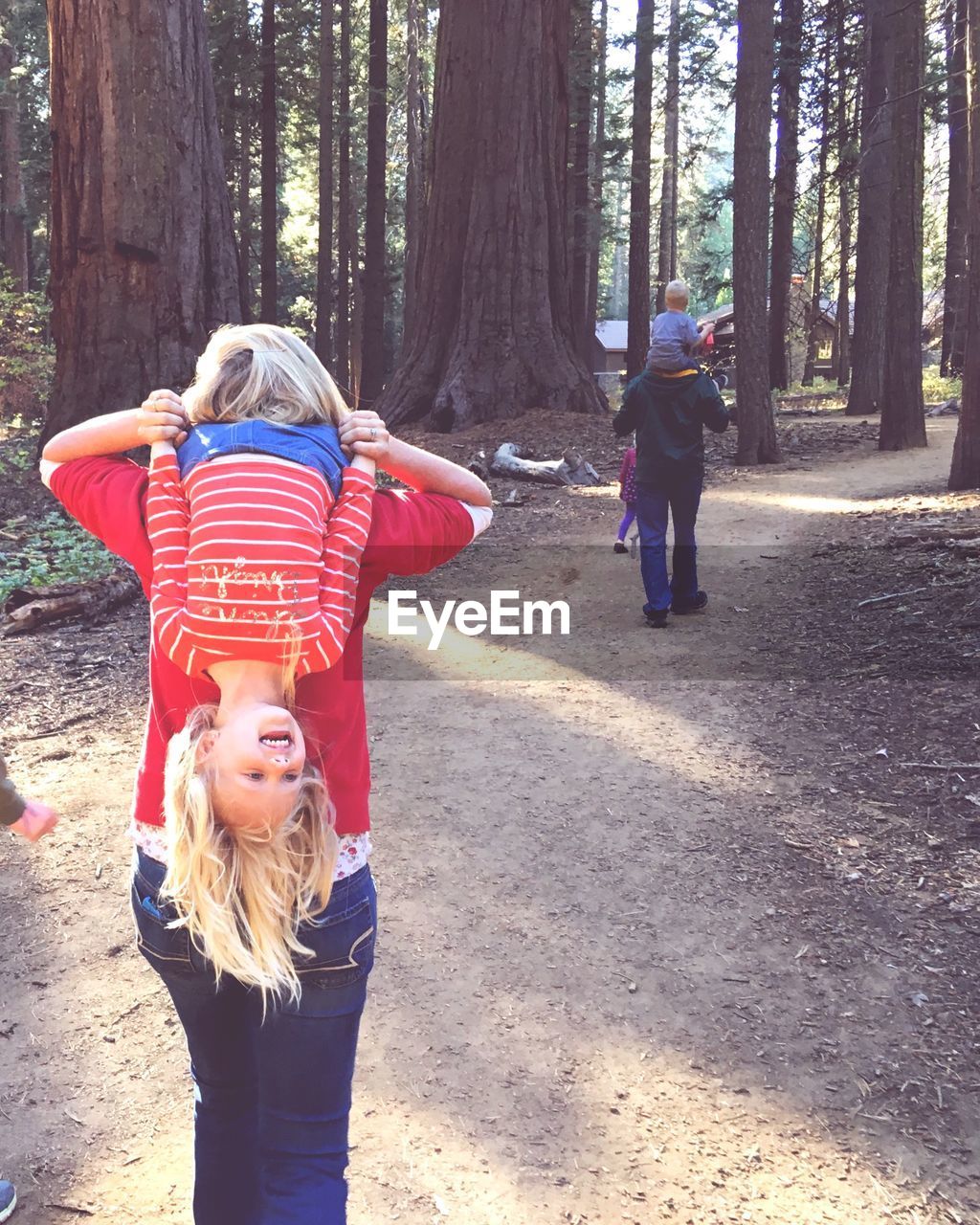 Rear view of parents piggybacking children while walking on footpath in forest