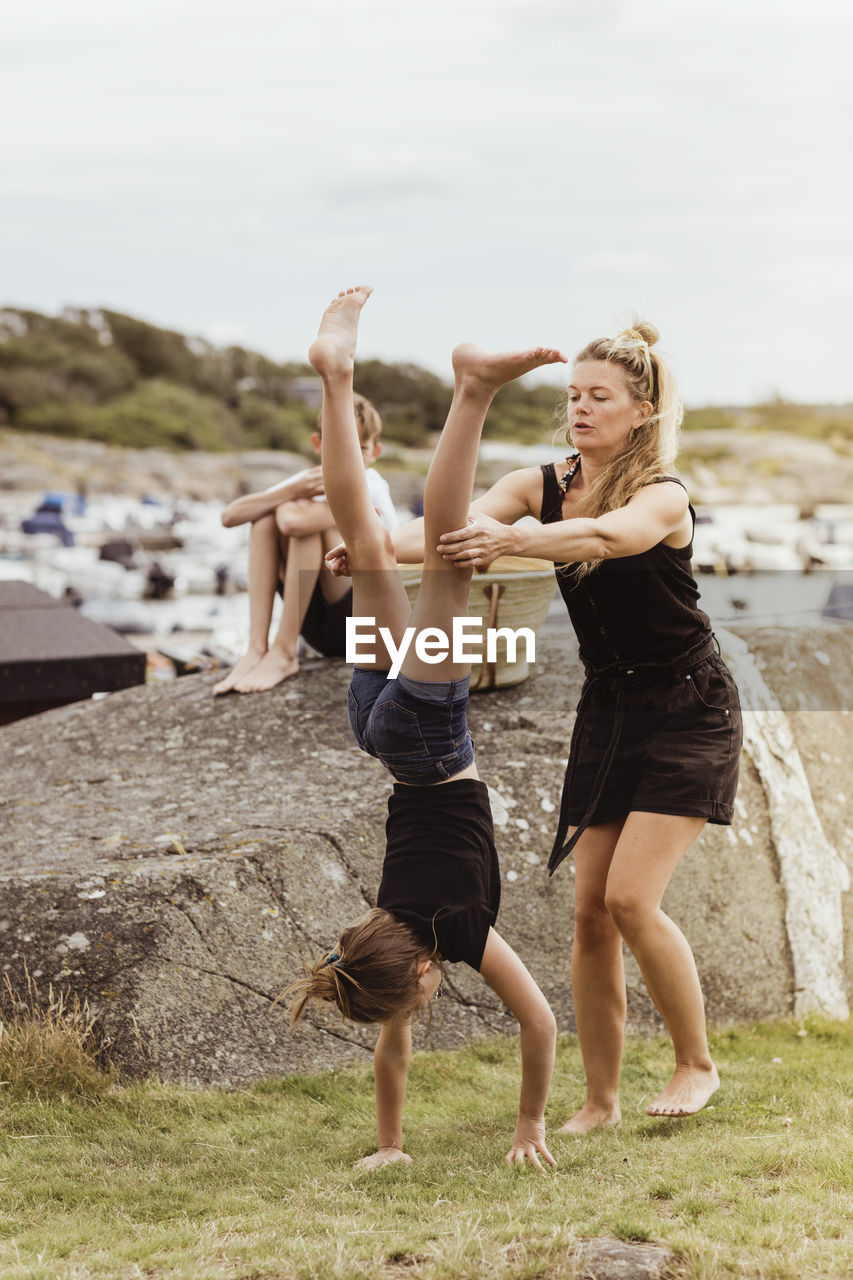 Mother helping daughter to do handstand on land at harbor