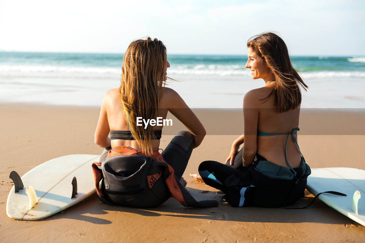 Rear view of female friends sitting at beach