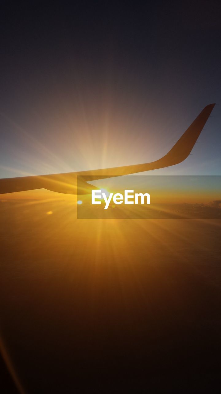 AIRPLANE FLYING OVER LANDSCAPE AGAINST SKY AT SUNSET