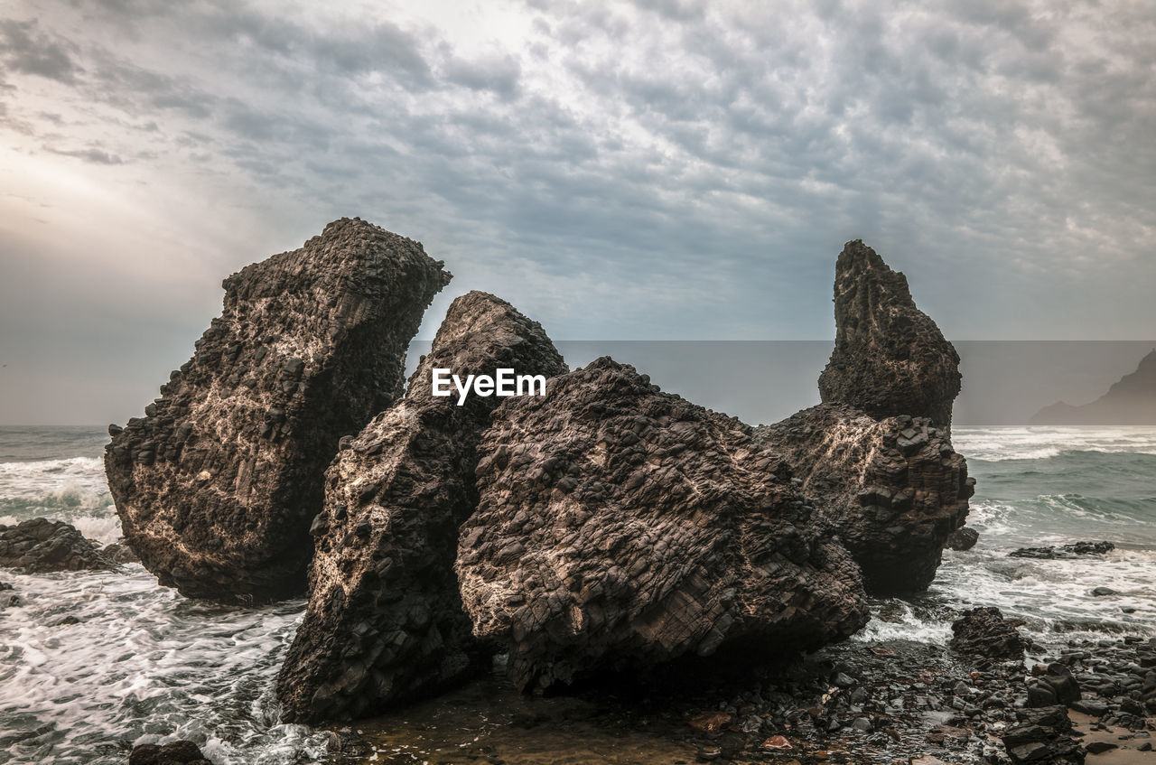 Rock formation on beach against sky