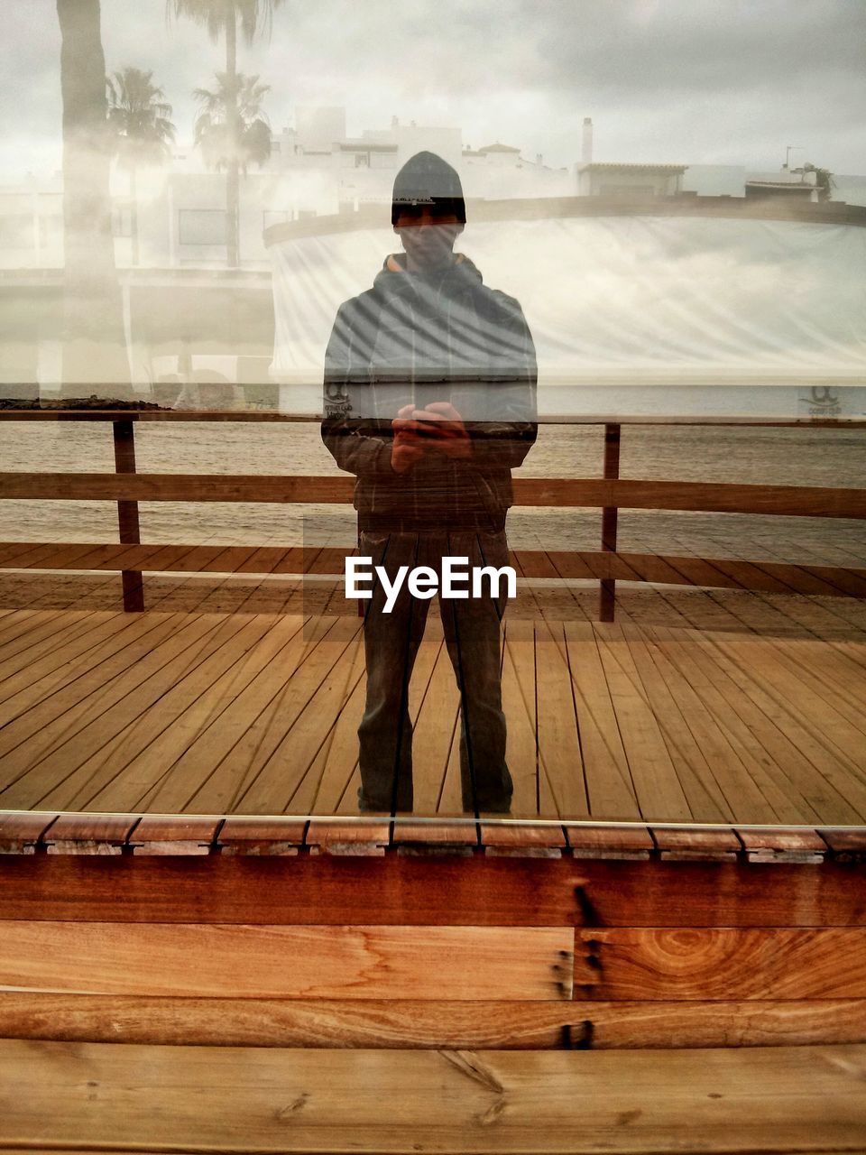 Reflection of man photographing on glass while standing over pier