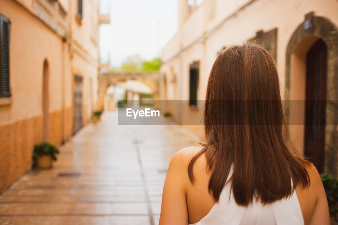 Rear view of woman standing on footpath amidst buildings in city