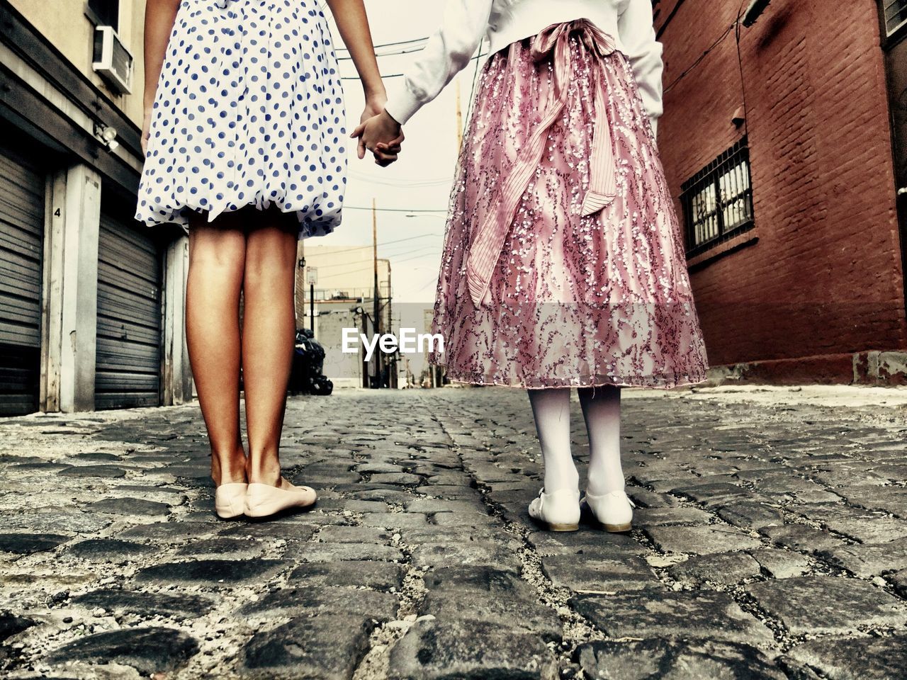 Low section of mother daughter holding hands while standing on cobblestone street