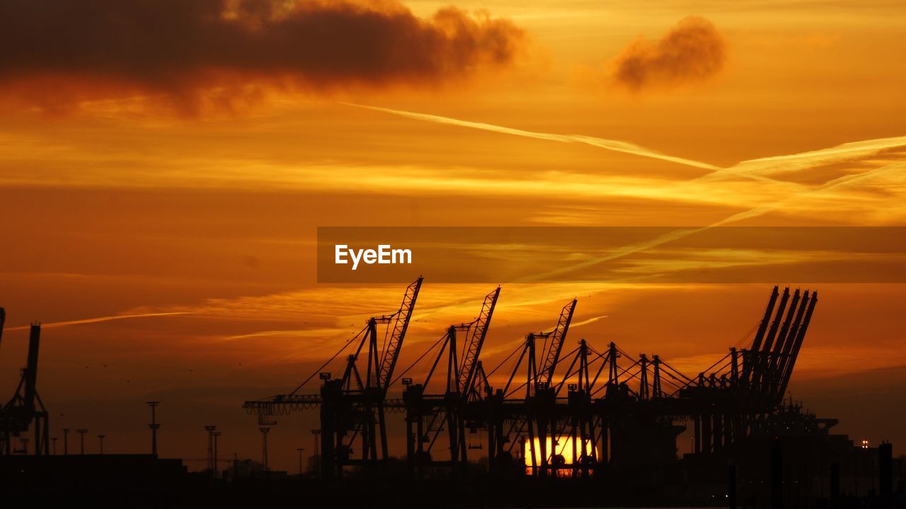 Silhouette cranes against orange sky during sunset