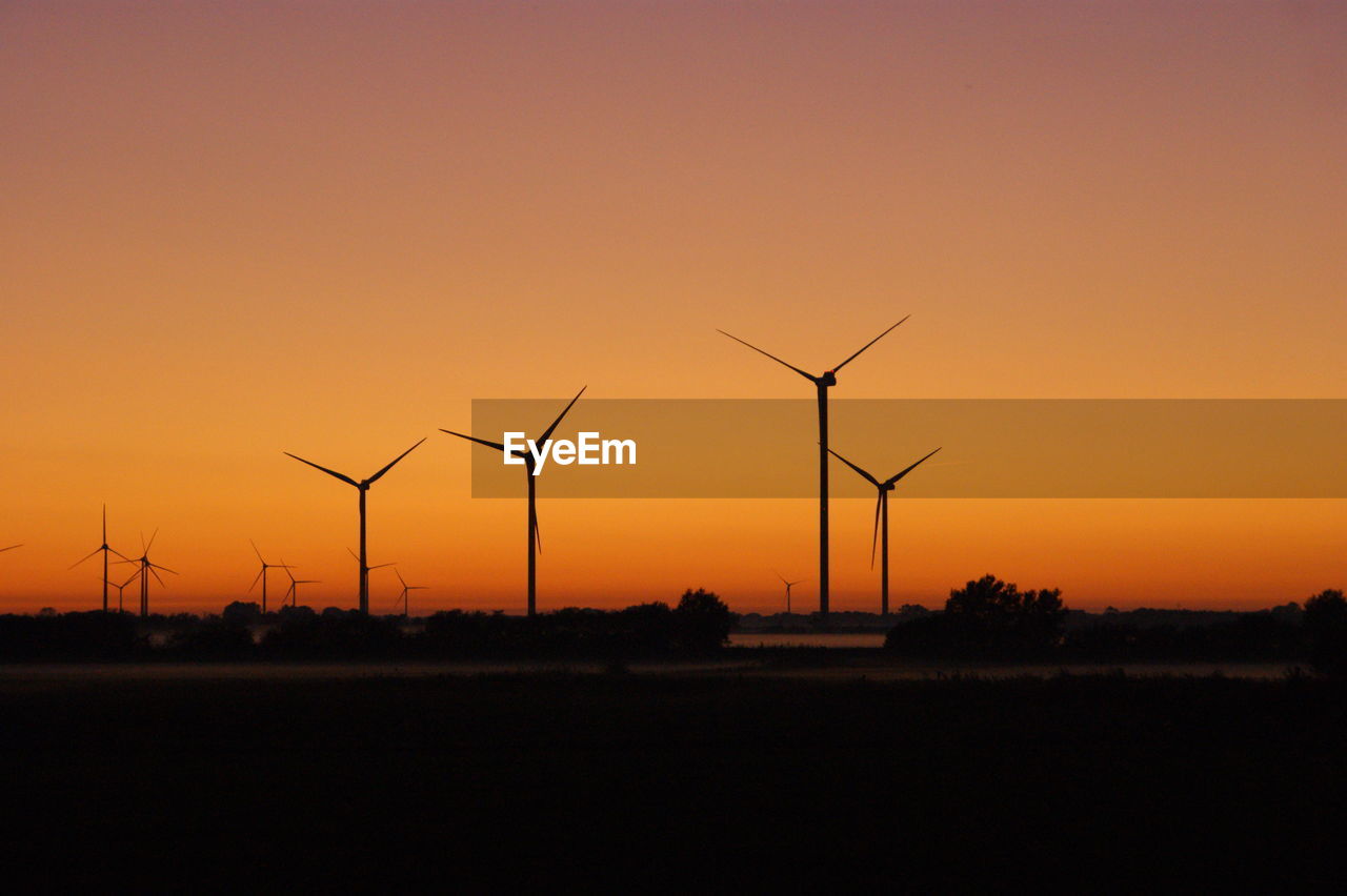 Silhouette wind turbines on field against sky during sunset