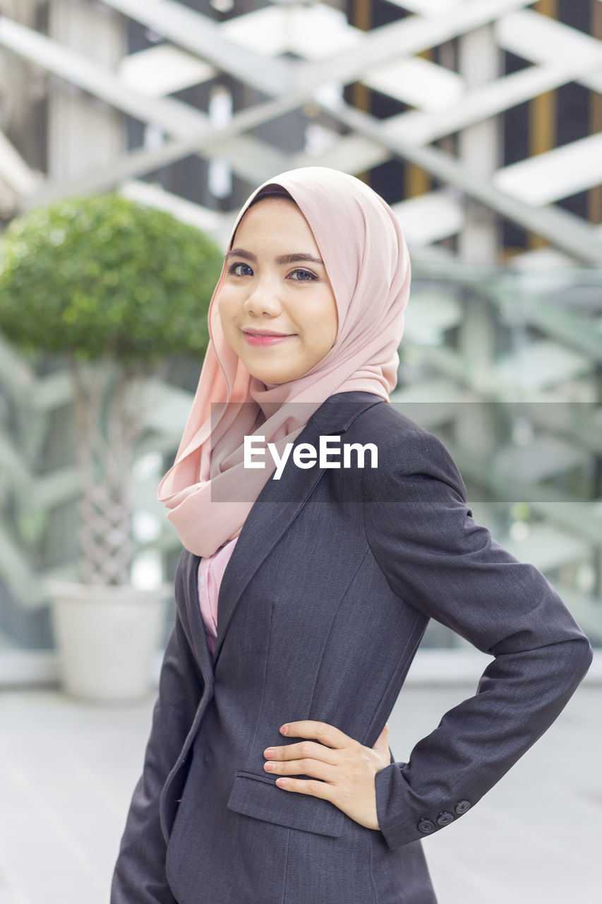 Portrait of confident businesswoman standing with hand on hip against modern office building