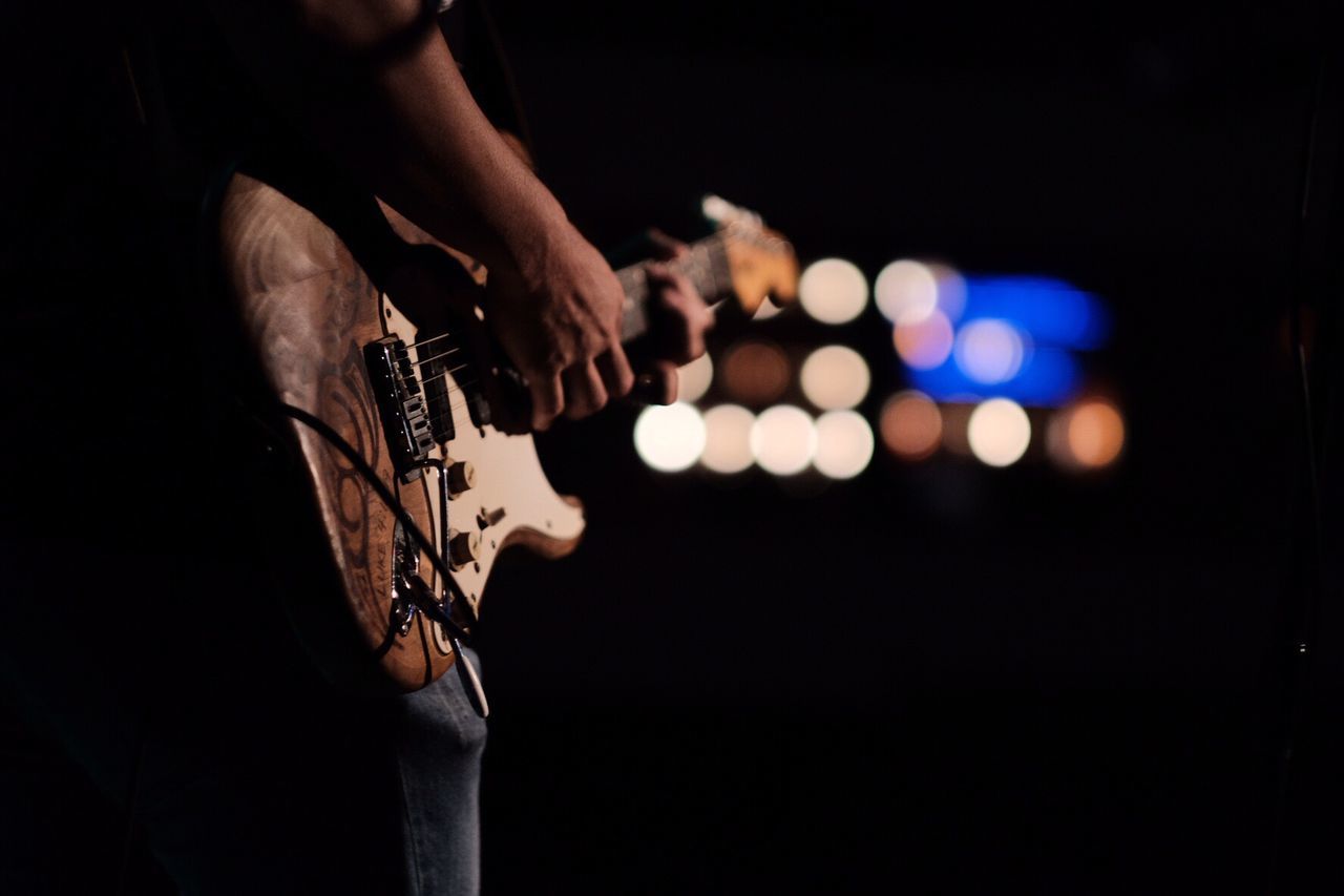 Midsection of person playing guitar at night