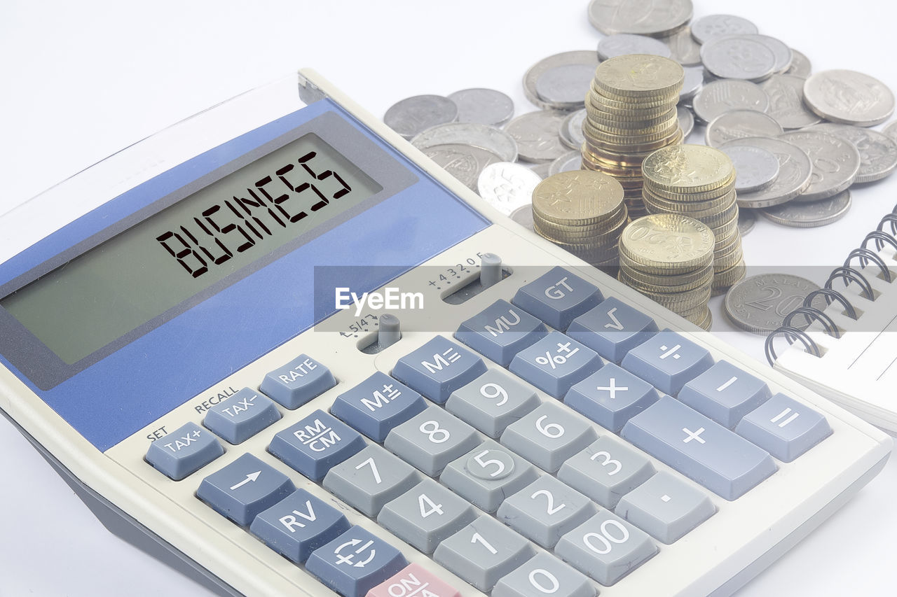 High angle view of coins and calculator by note pad on table