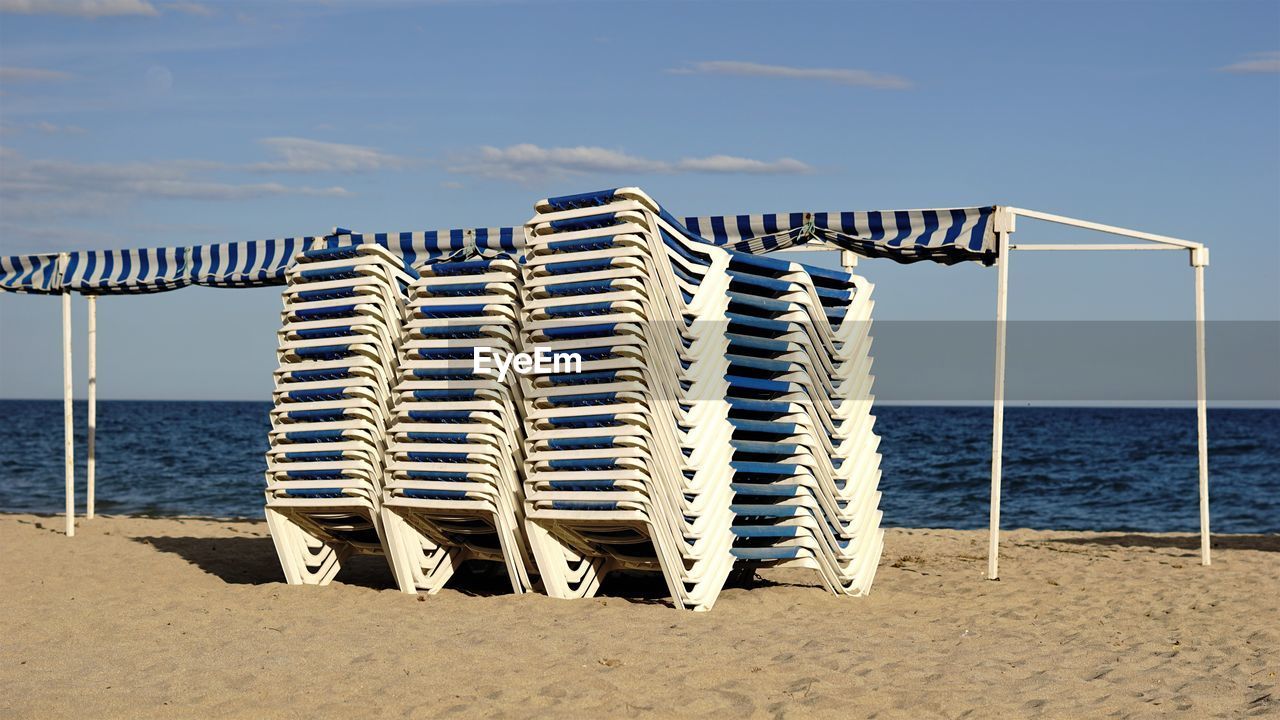 Hooded chairs on beach against sky