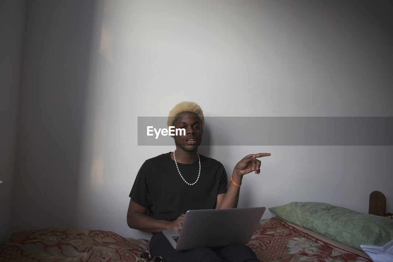 A young man sitting on a bed with a laptop