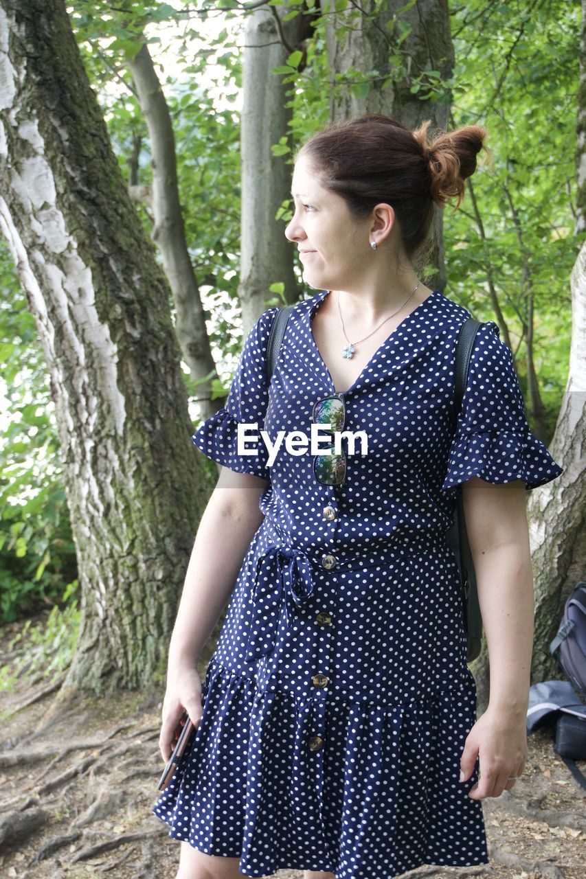 Young woman looking away while standing on tree trunk