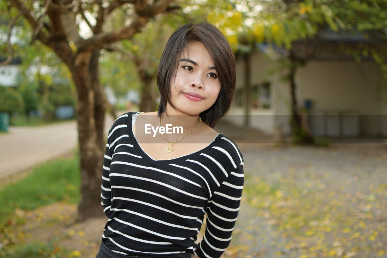 Beautiful young woman looking away while standing against trees in park