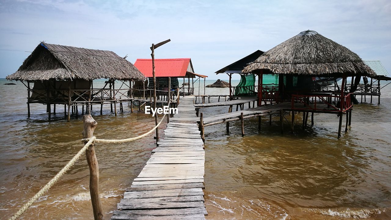 Stilt house by sea against sky